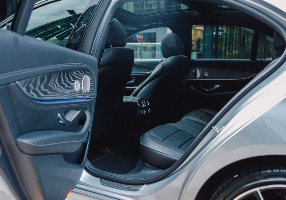 Interior view of a silver Mercedes E-Class displaying black leather seats and wood grain accents, open for a seamless executive transfer experience.