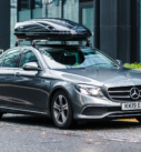 Grey Mercedes-Benz E-Class with a roof box parked on an urban street, prepared for city travel and transfers.