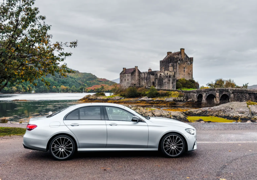 Silver Mercedes E-Class parked with Scotland's historic Eilean Donan Castle in the background, embodying a harmonious blend of modern travel and heritage.