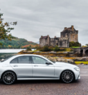 Silver Mercedes E-Class parked with Scotland's historic Eilean Donan Castle in the background, embodying a harmonious blend of modern travel and heritage.