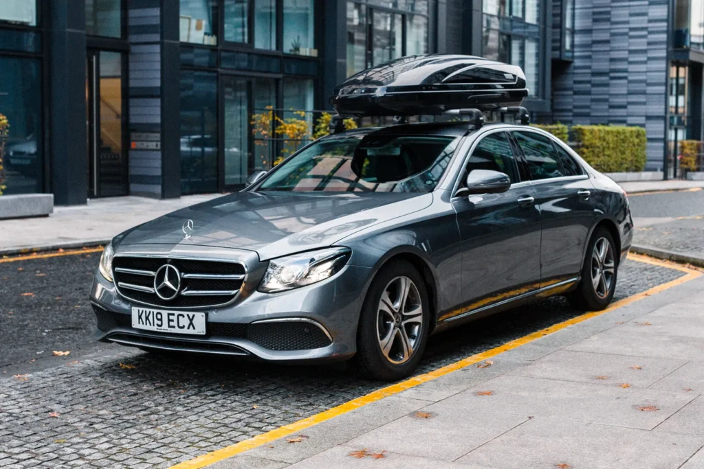 Grey Mercedes-Benz E-Class equipped with a Thule roof box parked in a modern city environment, ready for executive transfers.