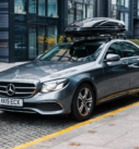 Grey Mercedes-Benz E-Class equipped with a Thule roof box parked in a modern city environment, ready for executive transfers.