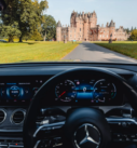 View from inside a Mercedes-Benz showcasing its advanced dashboard, with Glamis Castle standing majestically in the Scottish countryside ahead.