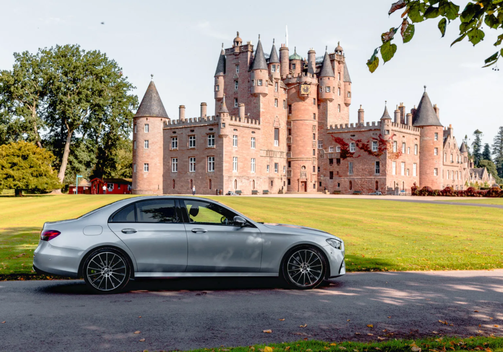 A silver Mercedes-Benz E-Class parked in front of the historic Glamis Castle in Scotland, symbolising executive travel in a land of heritage.