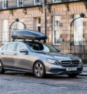 Grey Mercedes-Benz E-Class equipped with a Thule roof box, parked on a historic street in Edinburgh.