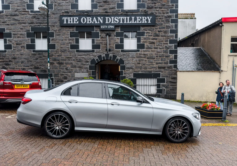 Mercedes E-Class parked by The Oban Distillery, Scotland, showcasing efficient transfer services.