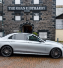 Mercedes E-Class parked by The Oban Distillery, Scotland, showcasing efficient transfer services.