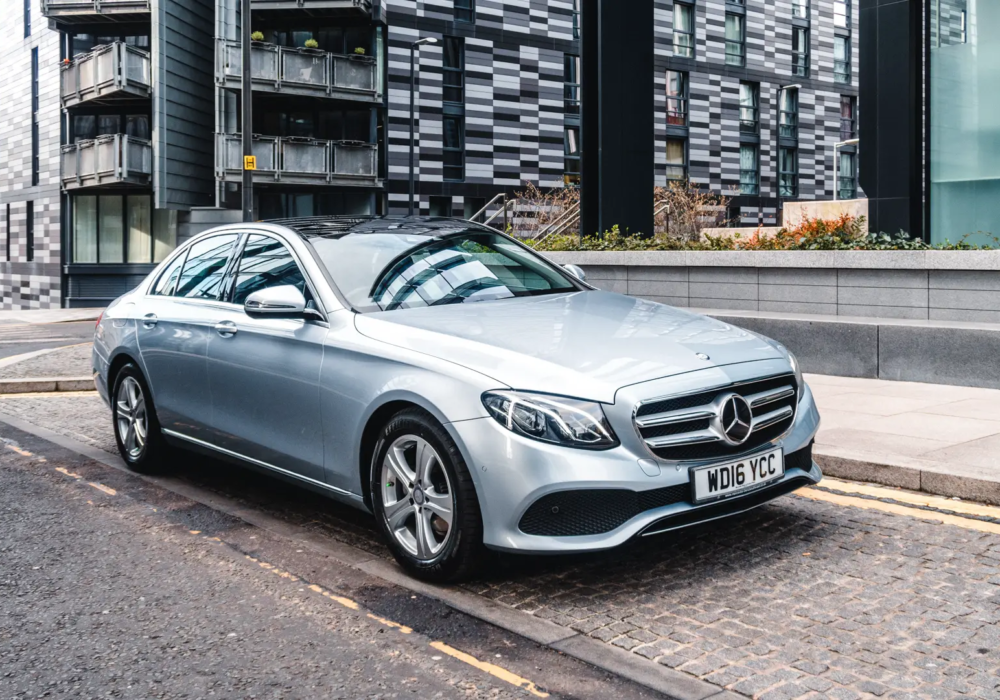 private-tour-mercedes-glasgow Silver Mercedes-Benz E-Class parked on a cobblestone street in Glasgow, ready for executive transport.